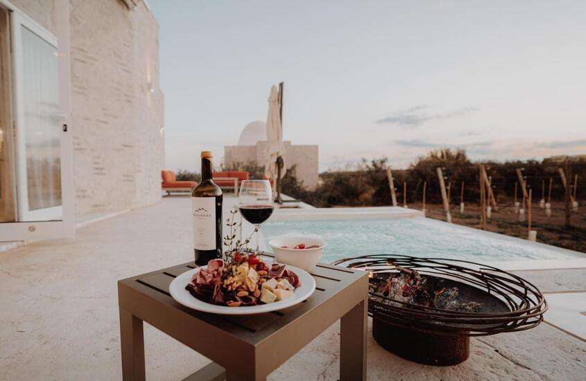 durante o dia, tábua de frios e vinho servidos em mesa de madeira, posta em frente a piscina ao ar livre