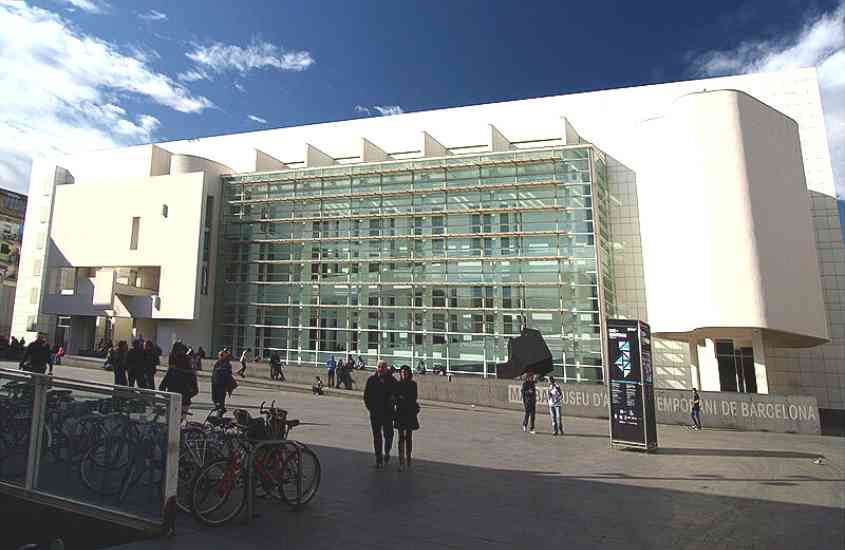 durante o dia, pessoas caminhando em frente a entrada de prédio branco, onde funciona museu em barcelona espanha