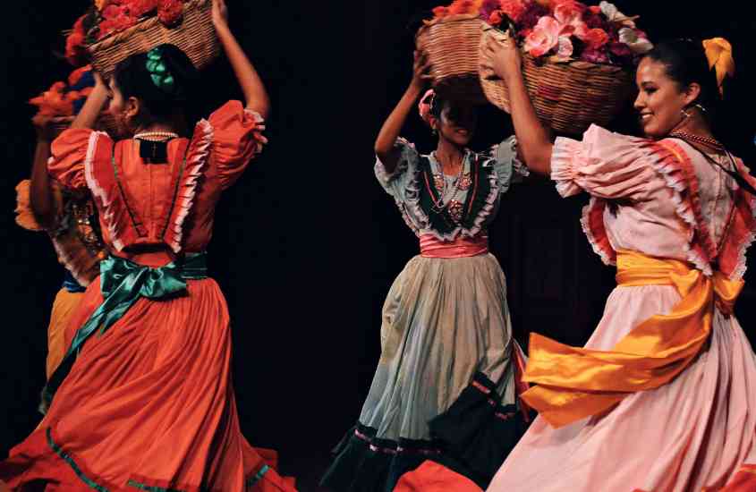 três dançarinas de flamenco, com vestidos coloridos, se apresentado em palco de teatro