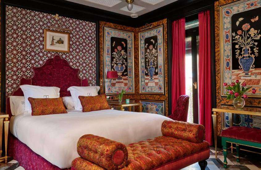 almofadas e travesseiros brancos em cima de cama de casal em suíte de hotel em sevilha decorado com papel de parede com estampas rosas e quadros com pinturas de vasos de flores