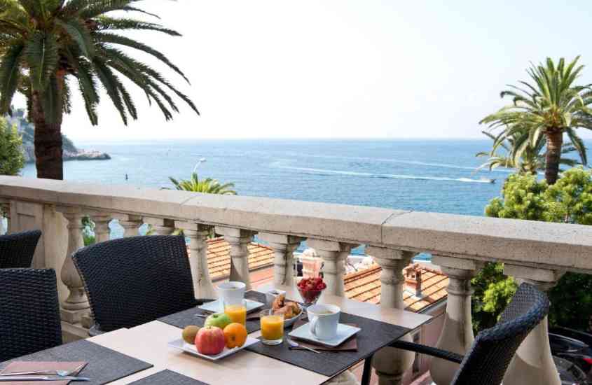 durante o dia, frutas, sucos e café em cima de mesa retangular, em varanda de hotel em nice com vista para o mar