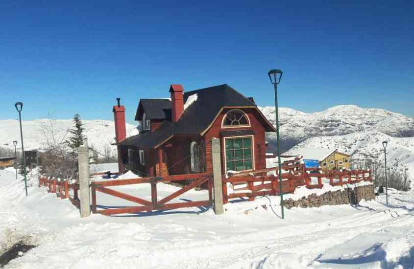 durante dia ensolarado, casa de madeira com telhado preto, rodeada por montanhas de neve
