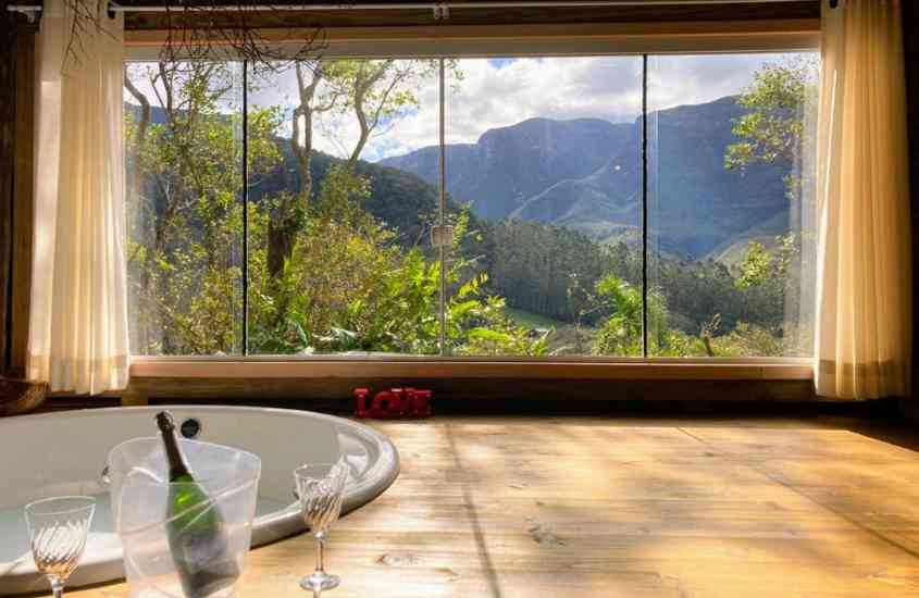 durante o dia, taças de vidro e garrafa de champanhe em borda de banheira, em camping de luxo com vista para as montanhas