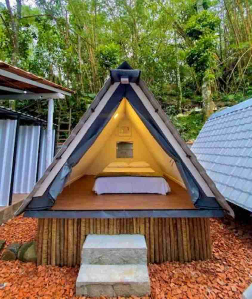 durante o dia, cama de casal dentro de tenda em formato triangular em jardim de camping de luxo no brasil