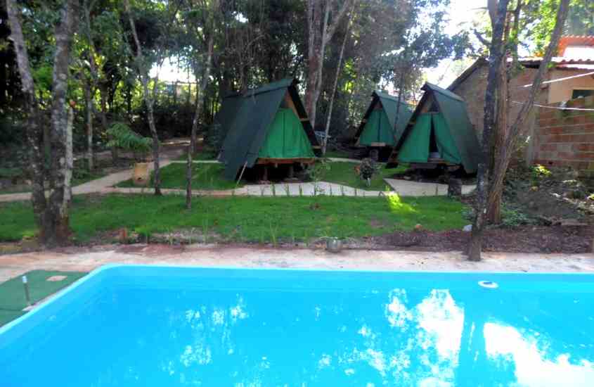 durante o dia, tendas de madeira em formato triangular, em frente a piscina de um dos hotéis glamping no brasil