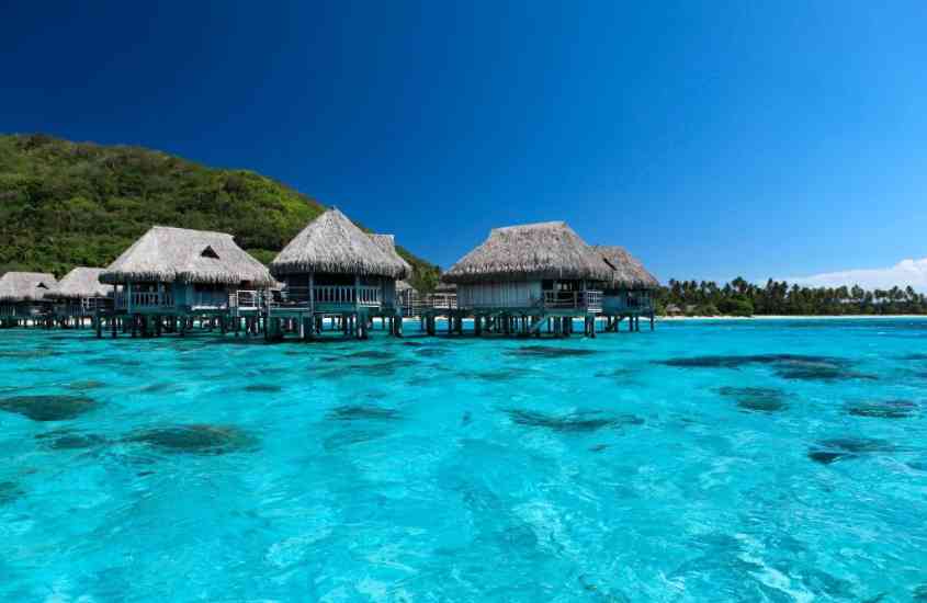 durante o dia, bangalôs com teto de palha sobre águas azuis em moorea, uma ilha paradisíaca da polinésia francesa