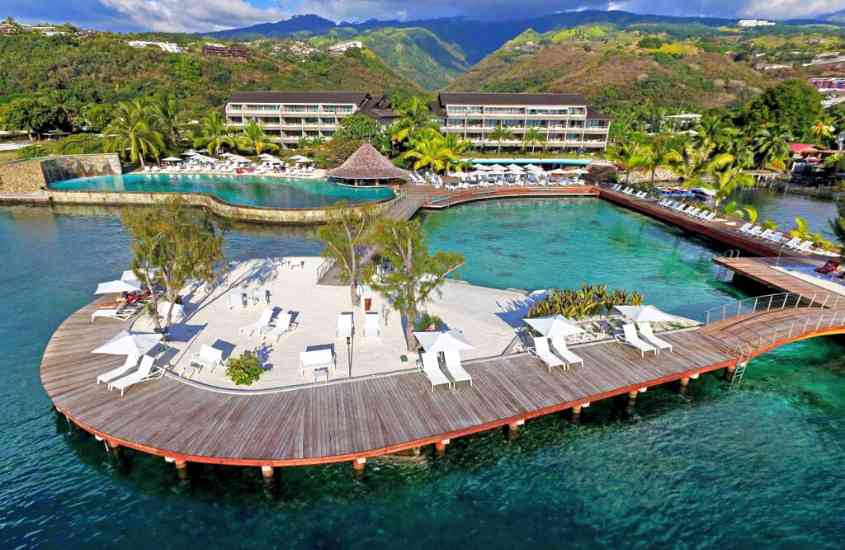 durante o dia, vista aérea de piscina e espreguiçadeiras em área de lazer ao livre de hotel na polinésia francesa com vista para o mar