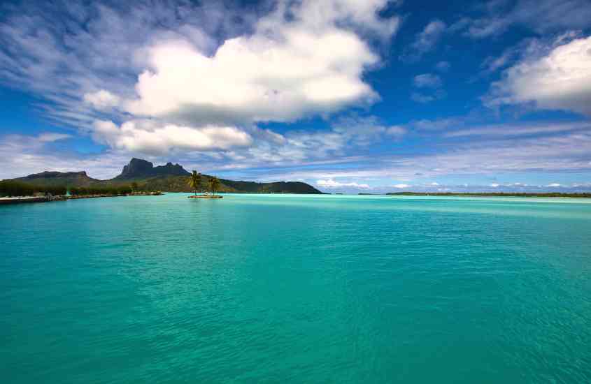 durante o dia, mar cristalino de uma das ilha na polinésia francesa e, ao fundo, montanhas