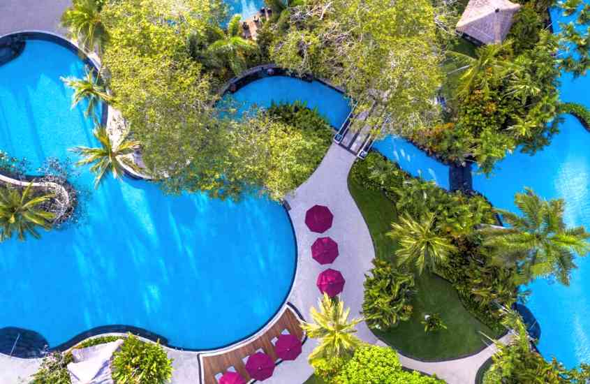 durante dia ensolarado, vista aérea de árvores ao redor de grande piscina em formato de lagoa em um dos melhores hotéis em bali