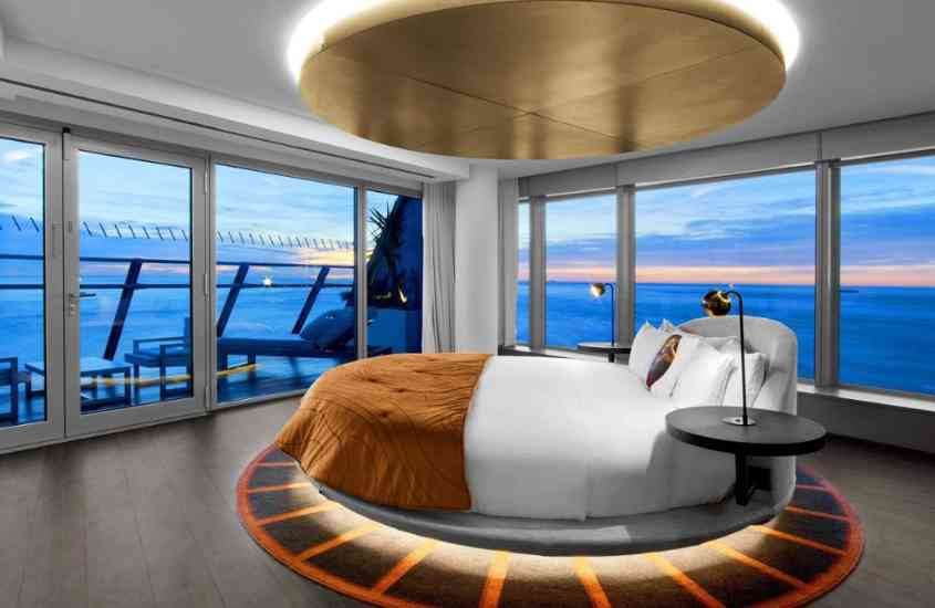 durante entardecer, cama redonda em suíte com janela panorâmica com vista para o mar