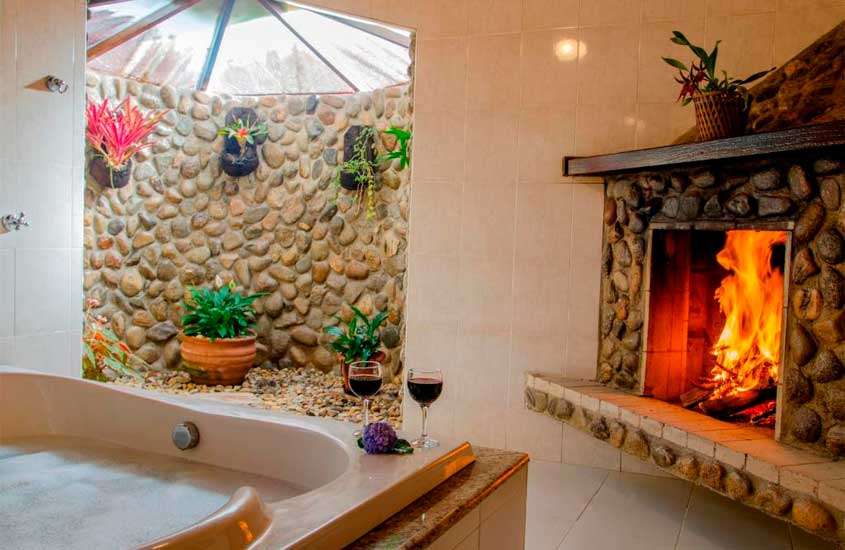Banheiro de suíte em pousada com banheira, taças de vinho, jardim de inverno e lareira.