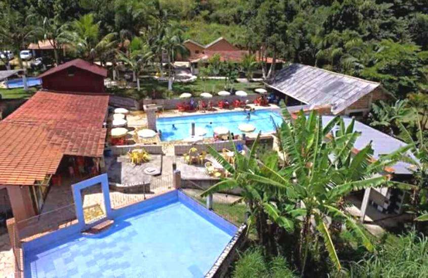durante dia ensolarado, vista aérea de árvores e piscina retangular ao ar livre em área de lazer de hotel fazenda no Rio de Janeiro barato
