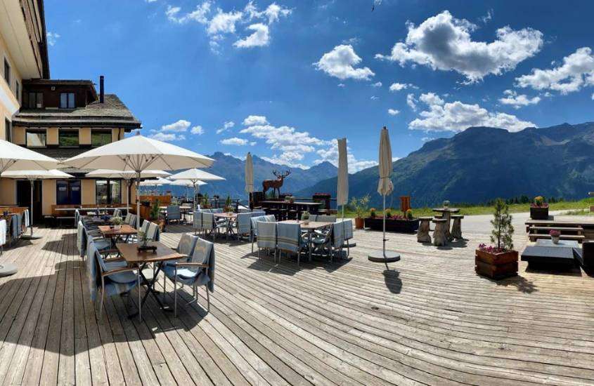durante dia ensolarado, mesas, cadeiras e guarda-sóis em restaurante ao ar livre de hotel em st. moritz com vista para as montanhas