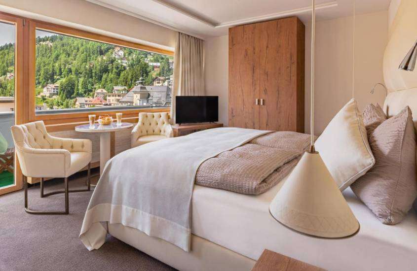 durante o dia, cama de casal, poltronas e guarda-roupa em suíte de hotel em st. moritz com vista para as montanhas