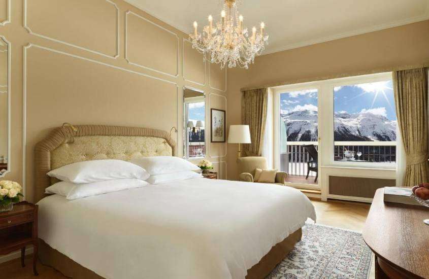 durante o dia, cama de casal, mesa de madeira e poltrona em suíte de hotel em st. moritz com varanda e vista para as montanhas