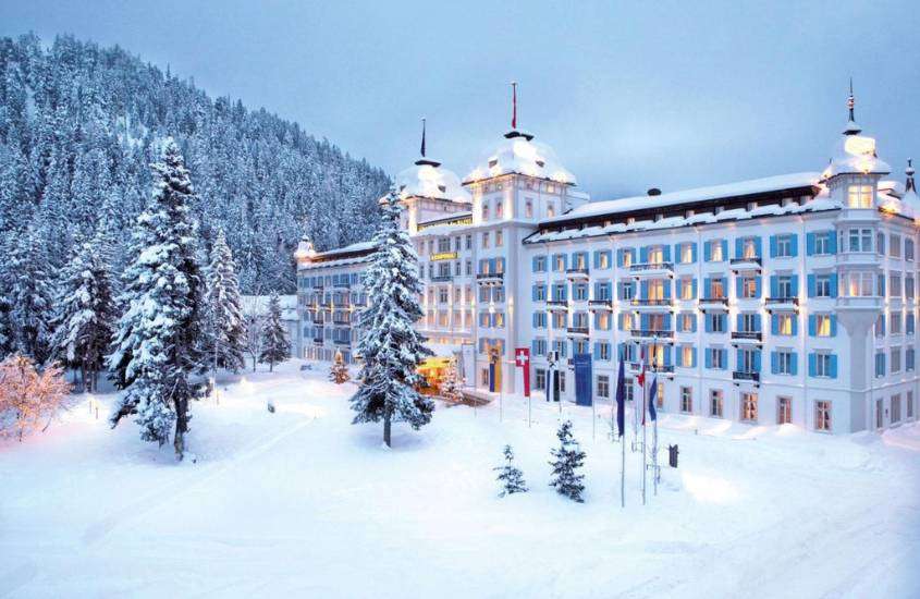 durante o dia nublado, montanha e árvores cobertas de neve em frente ao prédio branco de um hotel onde ficar em St. Moritz