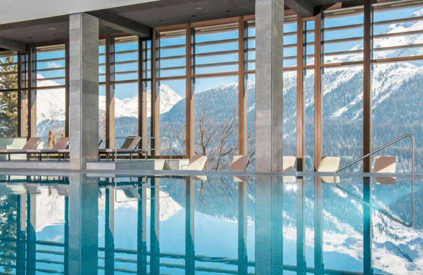 durante o dia, espreguiçadeiras em frente a piscina de área de lazer coberta com janelas panorâmicas com vista as montanhas