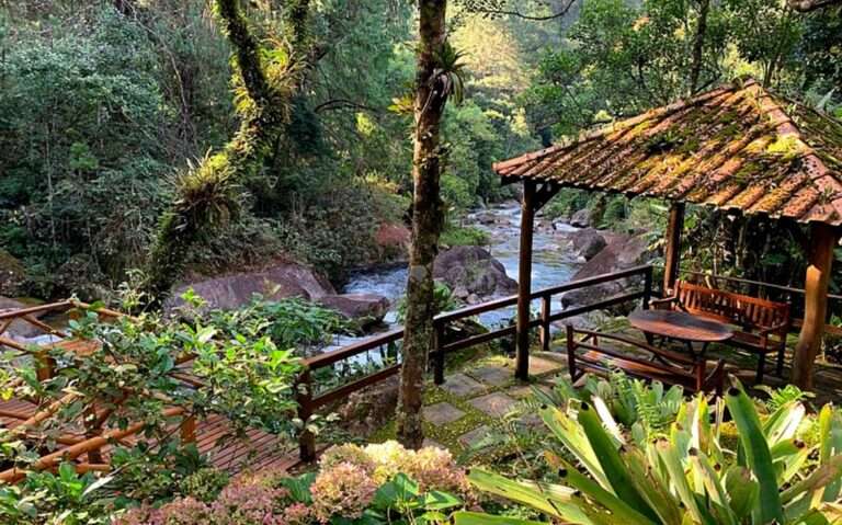 durante o dia, banquinhos e mesa de madeira em jardim em frente a cachoeira em área de lazer de uma das pousadas em visconde de Mauá pousadas em visconde de Mauá