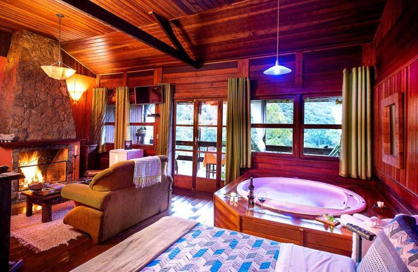 durante o dia, cama de casal, banheira de hidromassagem redonda, sofá e lareira em suíte de uma das pousadas românticas em Visconde de Mauá