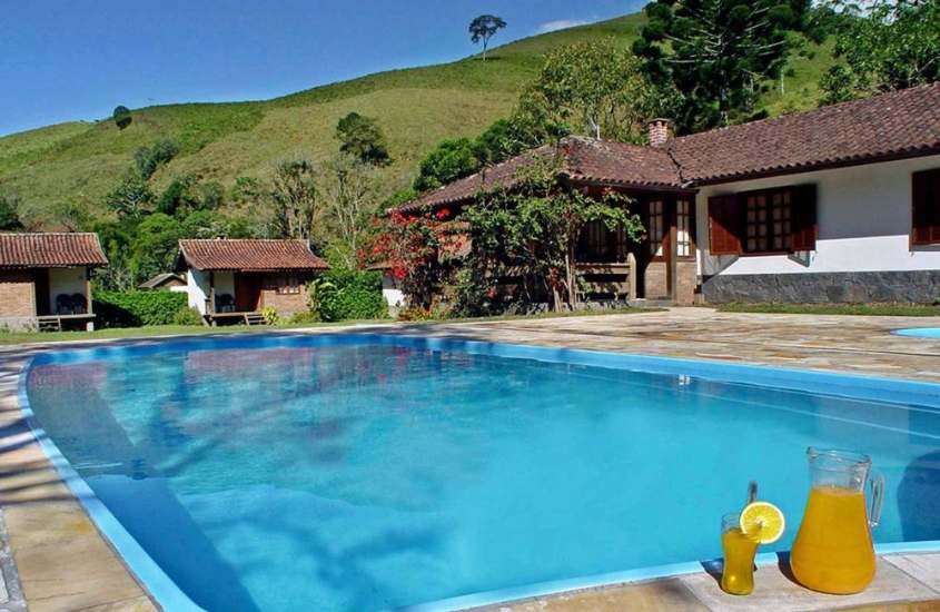 durante o dia, copo e garrafa de suco em borda de grande piscina ao ar livre com vista para as montanhas
