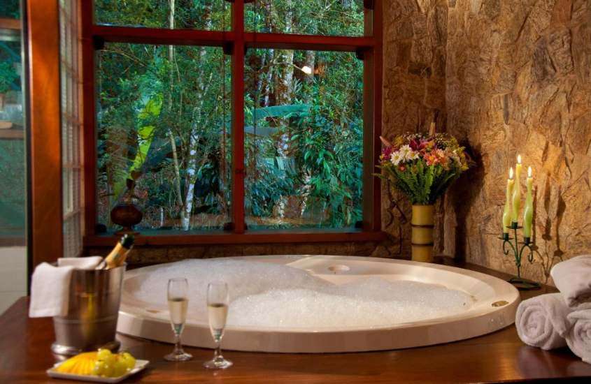 flores, velas e taças de champagne e uvas em borda de banheira redonda de suíte de uma das melhores pousadas em Visconde de Mauá com hidro