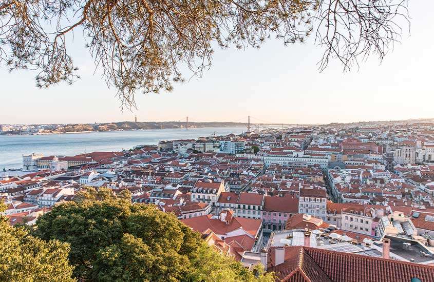 Durante o dia, vista panorâmica de casas típicas portuguesas com telhados laranjas e o mar ao fundo em Lisboa