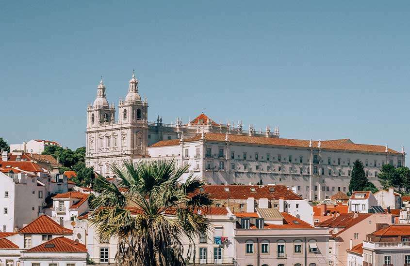 Vista panorâmica de Lisboa durante o dia, com destaque para as casas e catedral de Lisboa, sob céu azul