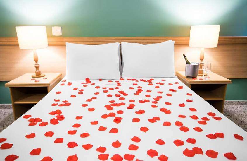 pétalas de rosas em cima de cama de casal forrada com lençol branco