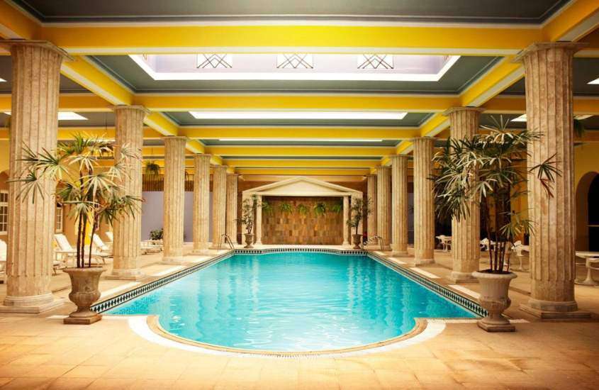 grande piscina rodeada por espreguiçadeiras e colunas romanas em área de lazer coberta de um dos melhores hotéis em poços de caldas