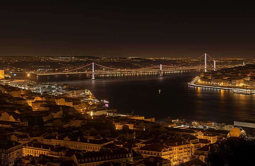 Durante a noite, vista das casas iluminadas às margens da água e ponte em Sintra