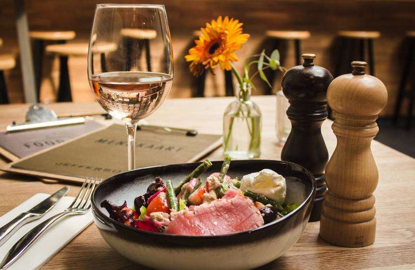 taça de vinho branco e prato com carne e salada em cima de mesa de madeira em um dos restaurantes em st moritz