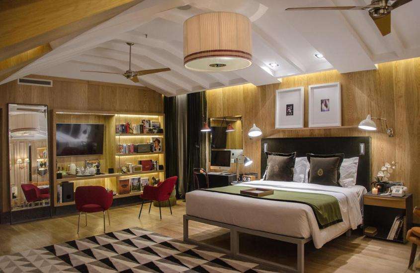 TV, poltronas vermelhas e cama de casal em suíte de melhores hotéis em Lisboa