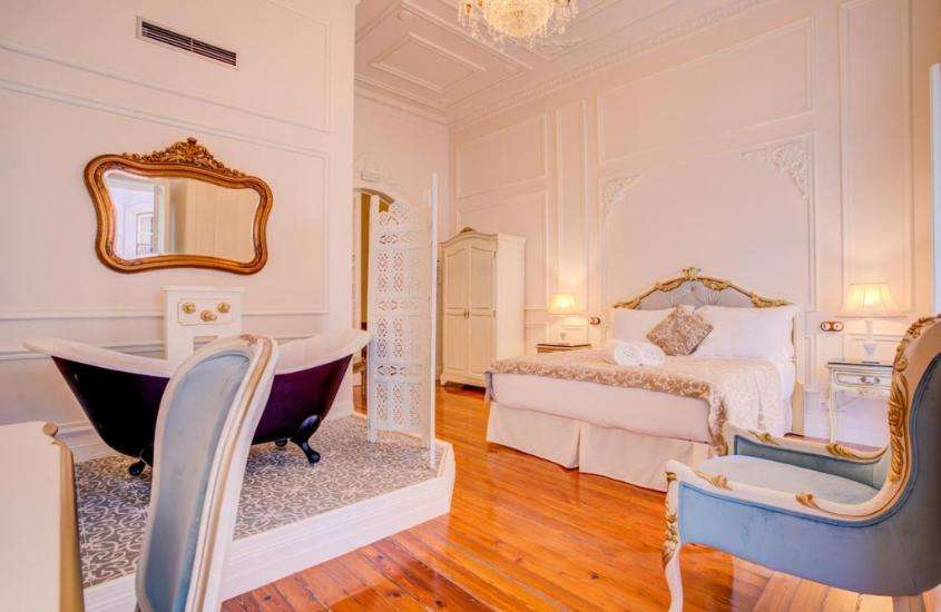 banheira vitoriana, poltrona e cama de casal em suíte de hotel em Lisboa com piso de madeira