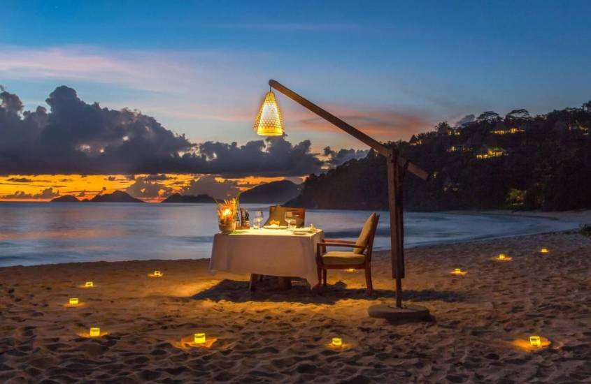 durante entardecer, cadeiras, mesa de jantar e velas em área de praia privativa de resort para passar a lua de mel em Seychelles