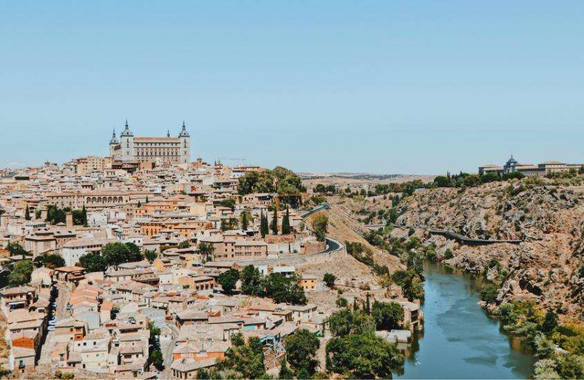 vista aérea durante o dia da cidade velha de Toledo, na Espanha, com muralhas medievais, palácios, igrejas e árvores às margens do rio