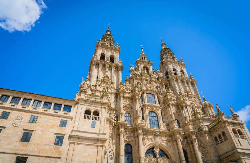 Durante o dia, vista da Catedral de Santiago de Compostela, uma obra arquitetônica que combina os estilos românico e gótico, com o céu azul ao fundo