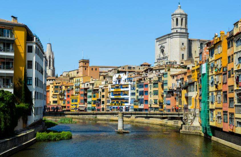 Durante o dia, vista aérea de casas coloridas em tons pastéis às margens do rio Onyar, no centro histórico de Girona