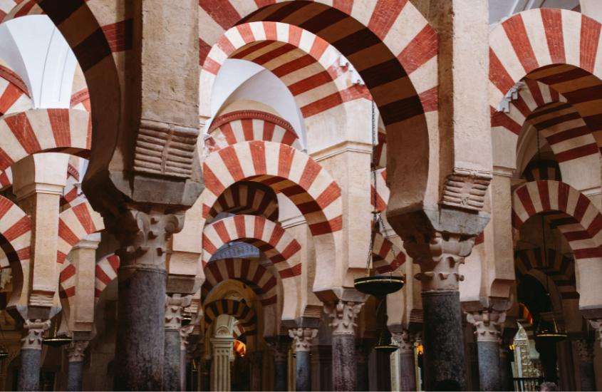 interior da Grande Mesquita de Córdova, ponto turístico da espanha com colunas em arco, e paredes decoradas com desenhos geométricos de azulejos coloridos e mosaicos