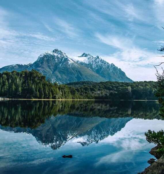 Durante o dia, paisagem de inverno em Bariloche com árvores cobertas de neve e montanhas nevadas refletidas em um lago cristalino
