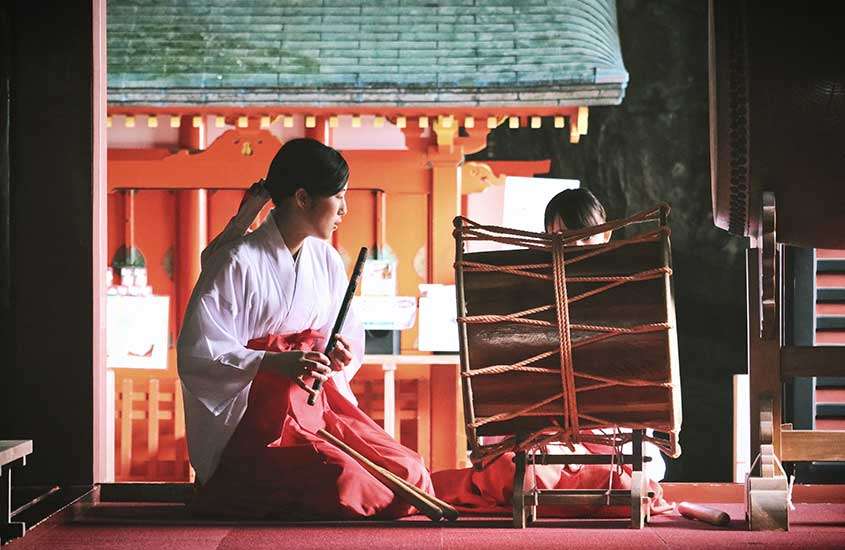 Mulher japonesa usando blusa branca e saia vermelha tocando flauta tradicional da cultura japonesa