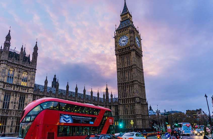 durante o entardecer, ônibus vermelho, carros e pessoas passando por rua em frente ao relógio do Big Ben em Londres, um dos melhores lugares para fazer intercâmbio