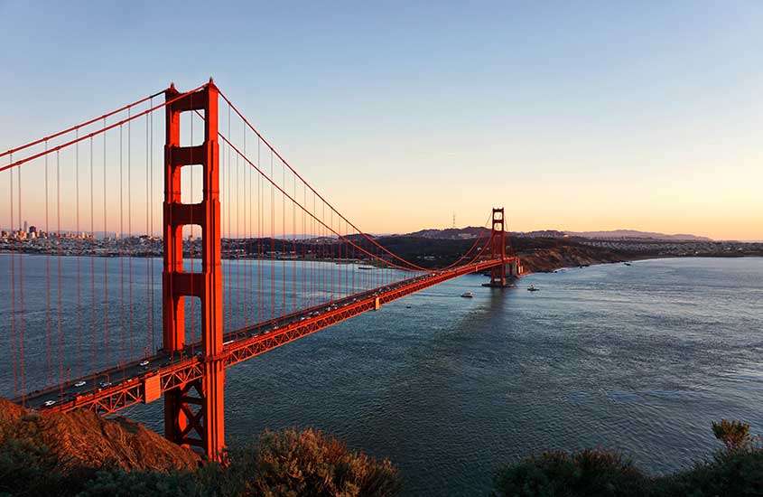 Durante o entardecer, vista aérea de carros passando em Golden Gate Bridge, ponte laranja sobre o mar em San Francisco, uma das melhores cidades para fazer intercâmbio