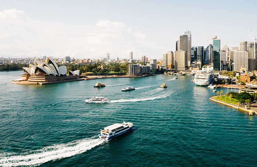 Durante o dia, vista aérea de barcos em movimento no rio em Sydney, com a Ópera de Sydney, com formato de concha, ao fundo