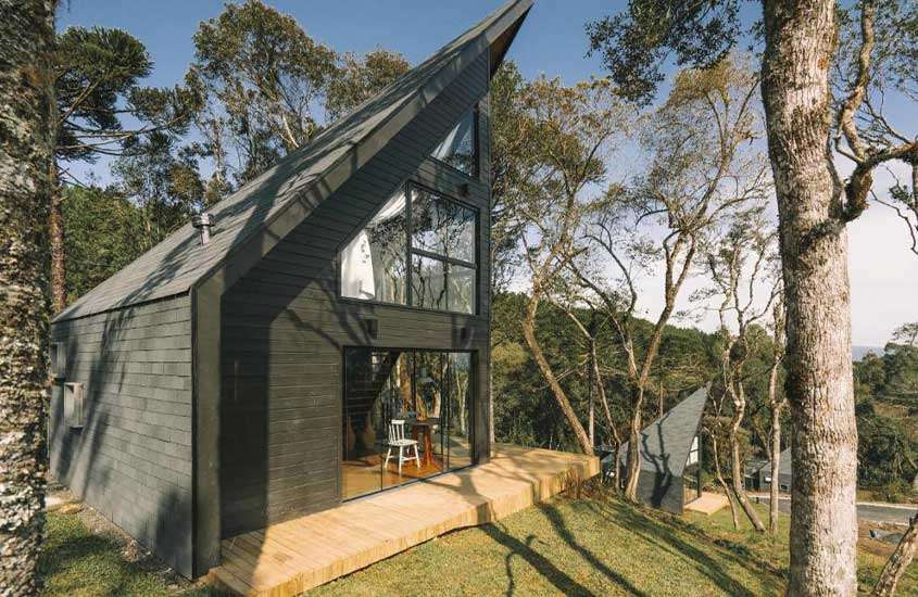 durante o dia, cabana preta de dois andares, com grandes janelas de vidro, rodeada por árvores