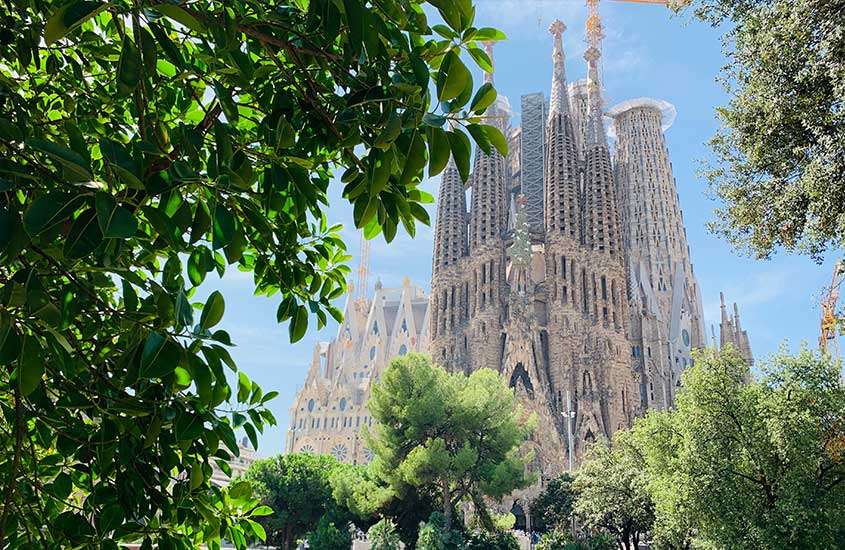 Durante o dia, árvores verdes em primeiro plano, e a majestosa basílica da Sagrada Família ao fundo, em Barcelona, na Espanha, um dos melhores países para fazer intercâmbio