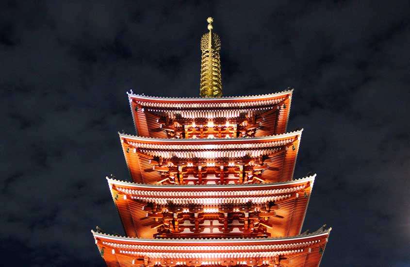 Vista noturna de templo japonês em estilo arquitetônico marrom com telhado em forma de ponta, visto de baixo para cima