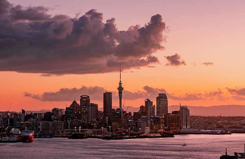 Durante entardecer alaranjado, vista aérea de prédios modernos e arranha-céus às margens do mar em Auckland, Nova Zelândia