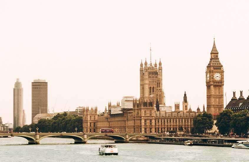 Durante o dia, barco turístico navegando pelo rio Tâmisa com vista para o Big Ben e o Palácio de Westminster, em um dos melhores lugares para ficar em Londres.