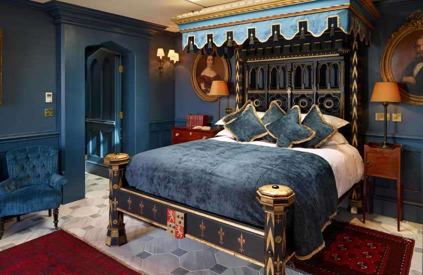 cama de casal e poltrona em suíte de hotel em Londres com paredes azuis, decoradas com antiguidades.