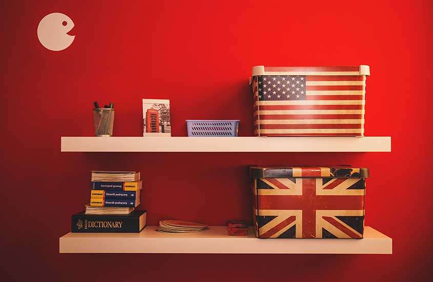 Prateleiras brancas em parede vermelha exibindo caixas decorativas dos Estados Unidos e Londres, dicionários e fotos